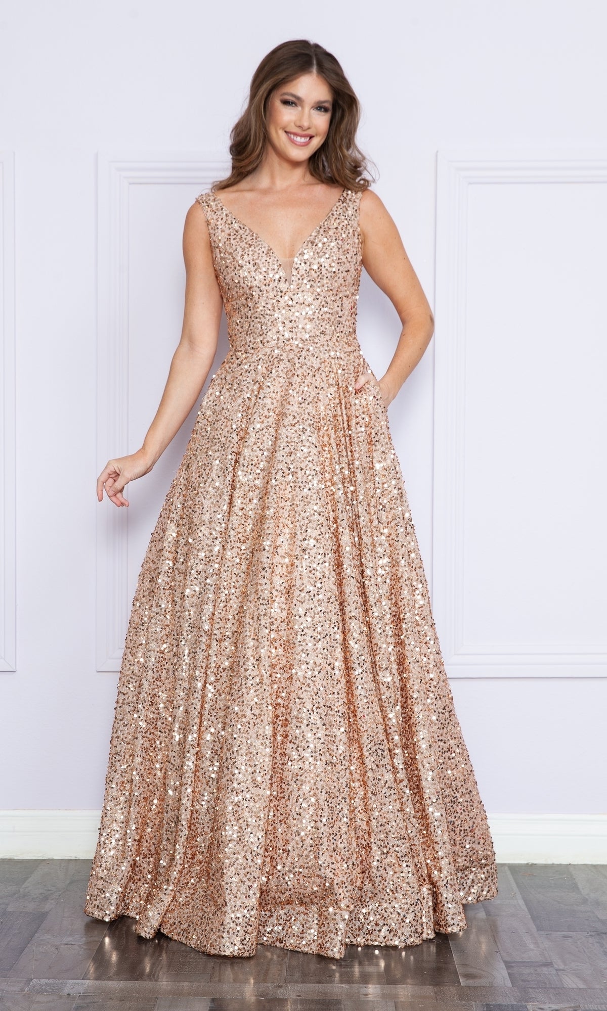 A woman stands indoors, smiling at the camera in the Long Black Sequin A-Line Prom Dress 9168, a sleeveless floor-length gown with a deep V-neckline.